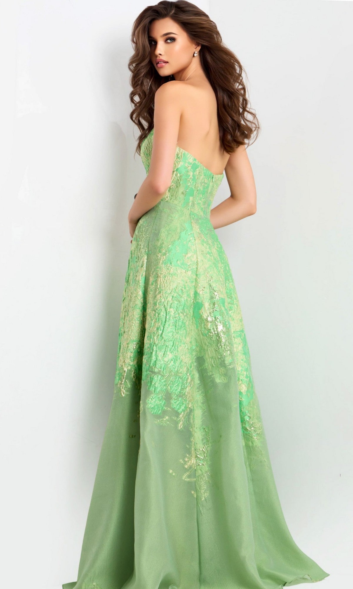 A woman with long brown hair models the Jovani 46260, a strapless green long prom dress with an A-line skirt and subtle metallic accents, standing against a plain light background.